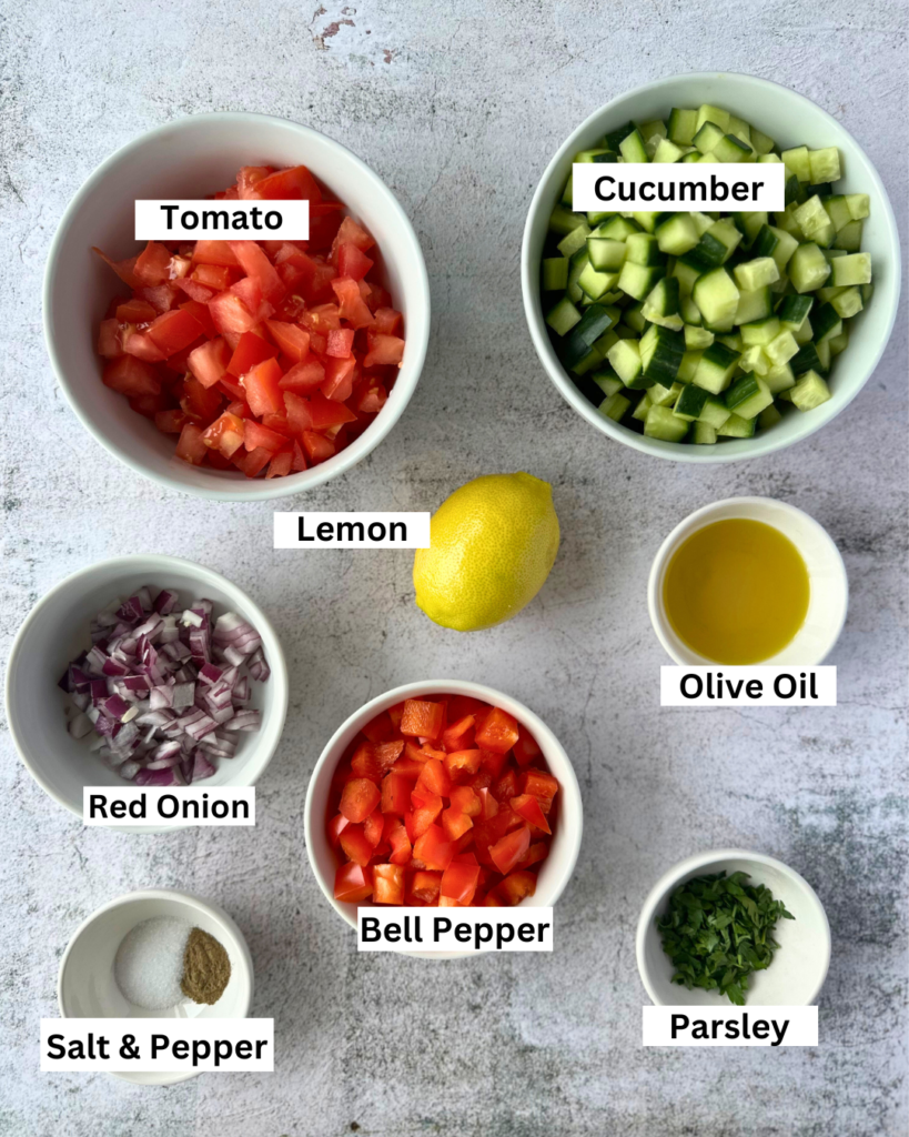 Israeli salad ingredients in separe bowls: diced cucumber, diced tomato, diced bell pepper, chopped red onion and fresh parsley. Whole lemon, salt and pepper and olive oil.